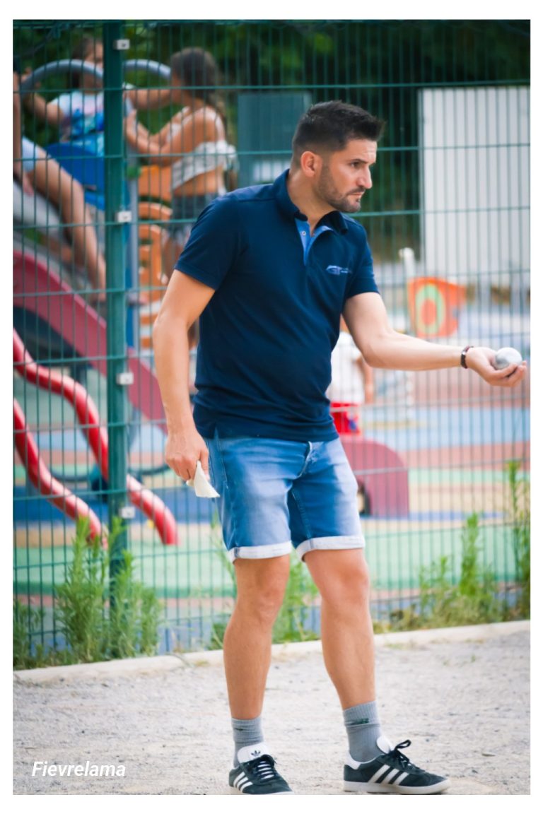 Un joueur en polo bleu se concentre, une boule dans la main, sur le terrain.