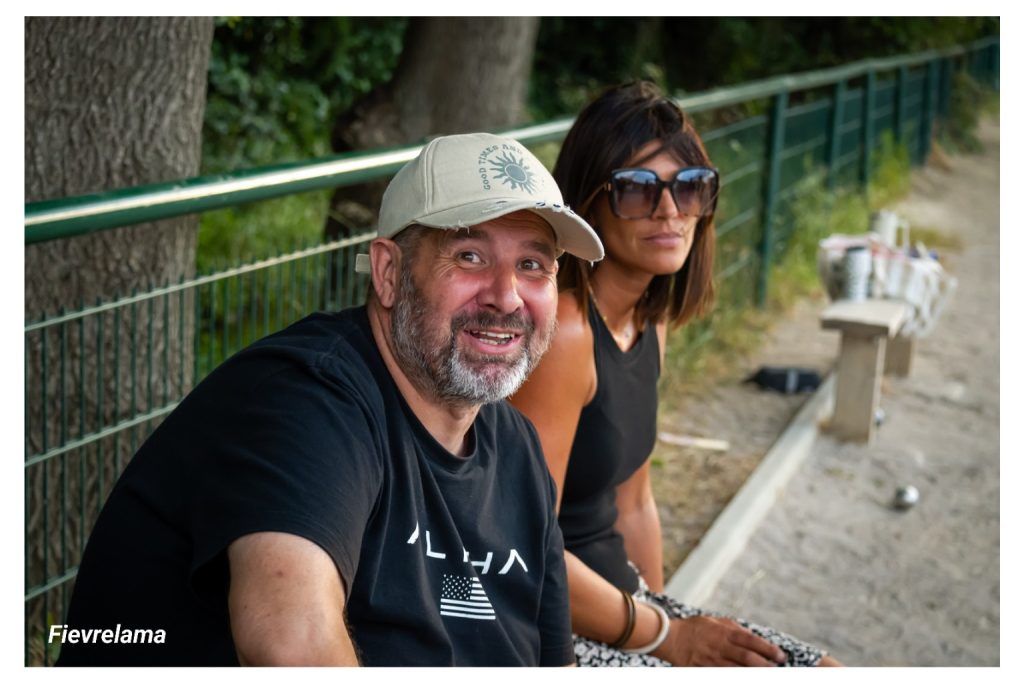 Deux membres assis au bord du terrain, un homme souriant et une femme portant des lunettes de soleil.