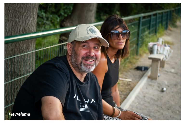 Deux membres assis au bord du terrain, un homme souriant et une femme portant des lunettes de soleil.