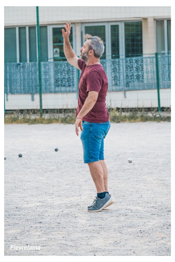 Un joueur en tee-shirt bordeaux termine son geste de lancer, le bras levé.