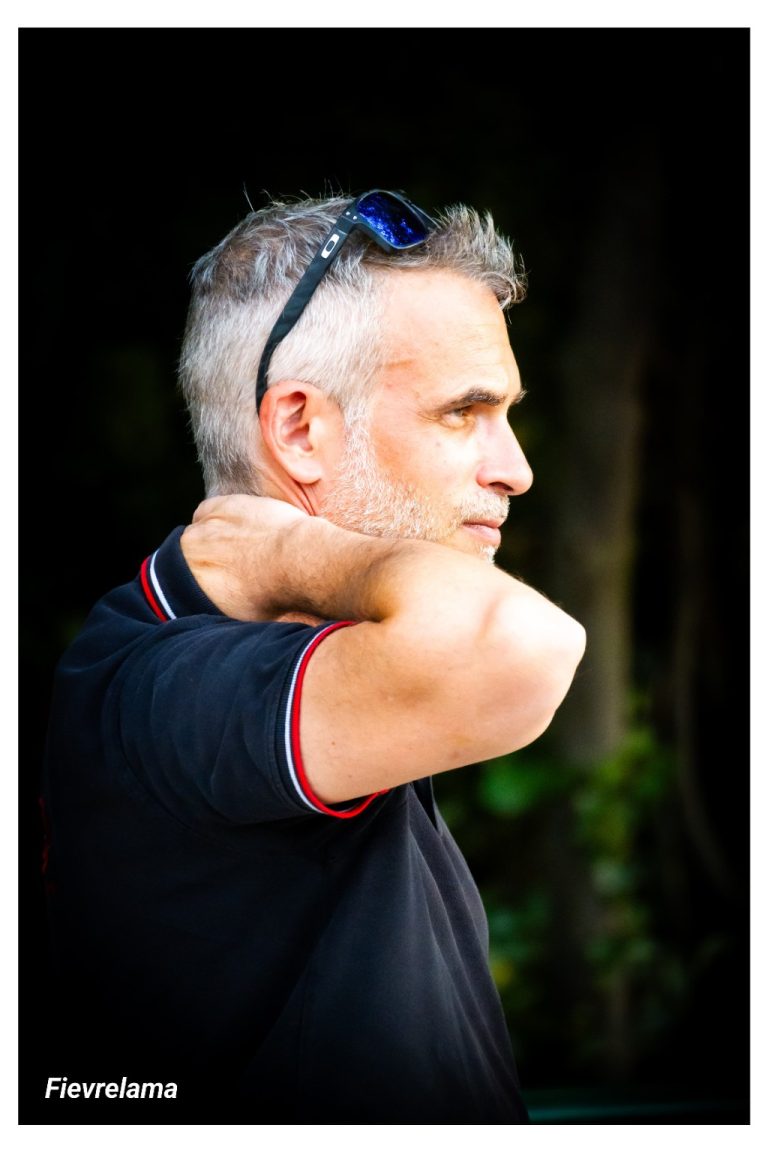 Portrait de profil d’un membre en polo sombre, les lunettes sur la tête et la main derrière la nuque.