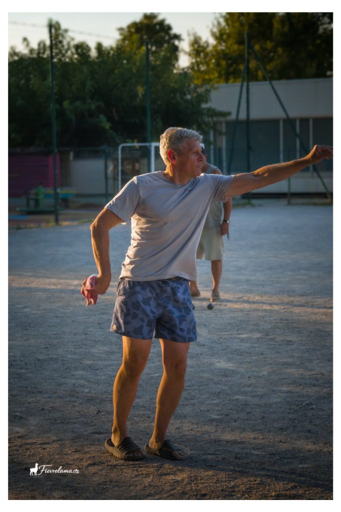 Un joueur en tee-shirt gris tend le bras après son lancer, dans la lumière du soir.