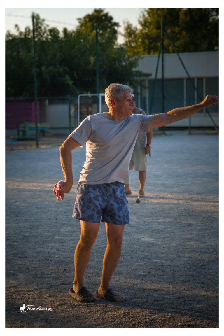 Un joueur en tee-shirt gris tend le bras après son lancer, dans la lumière du soir.
