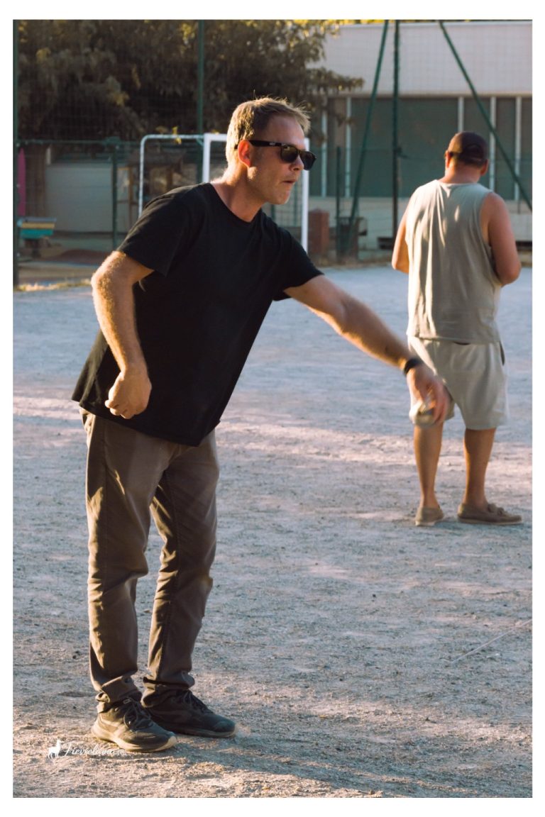 Un joueur en tee-shirt noir et lunettes de soleil s’apprête à lancer une boule en fin de journée.