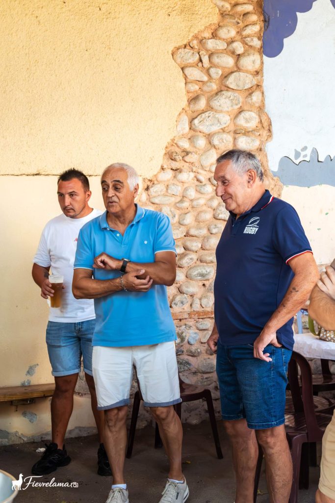 Trois adhérents du club de pétanque en discussion devant un mur en galets