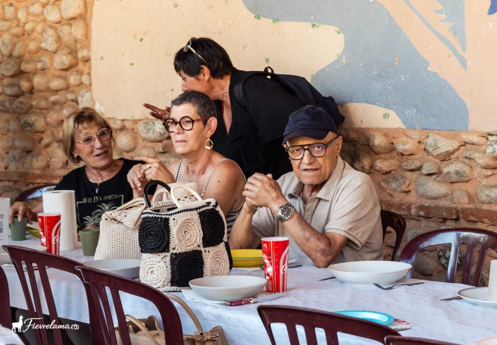 Convives attablés devant la fresque et le mur en pierre du préau